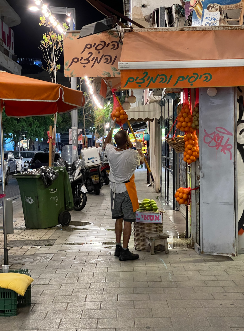A man taking down bundles of oranges, closing down his shop